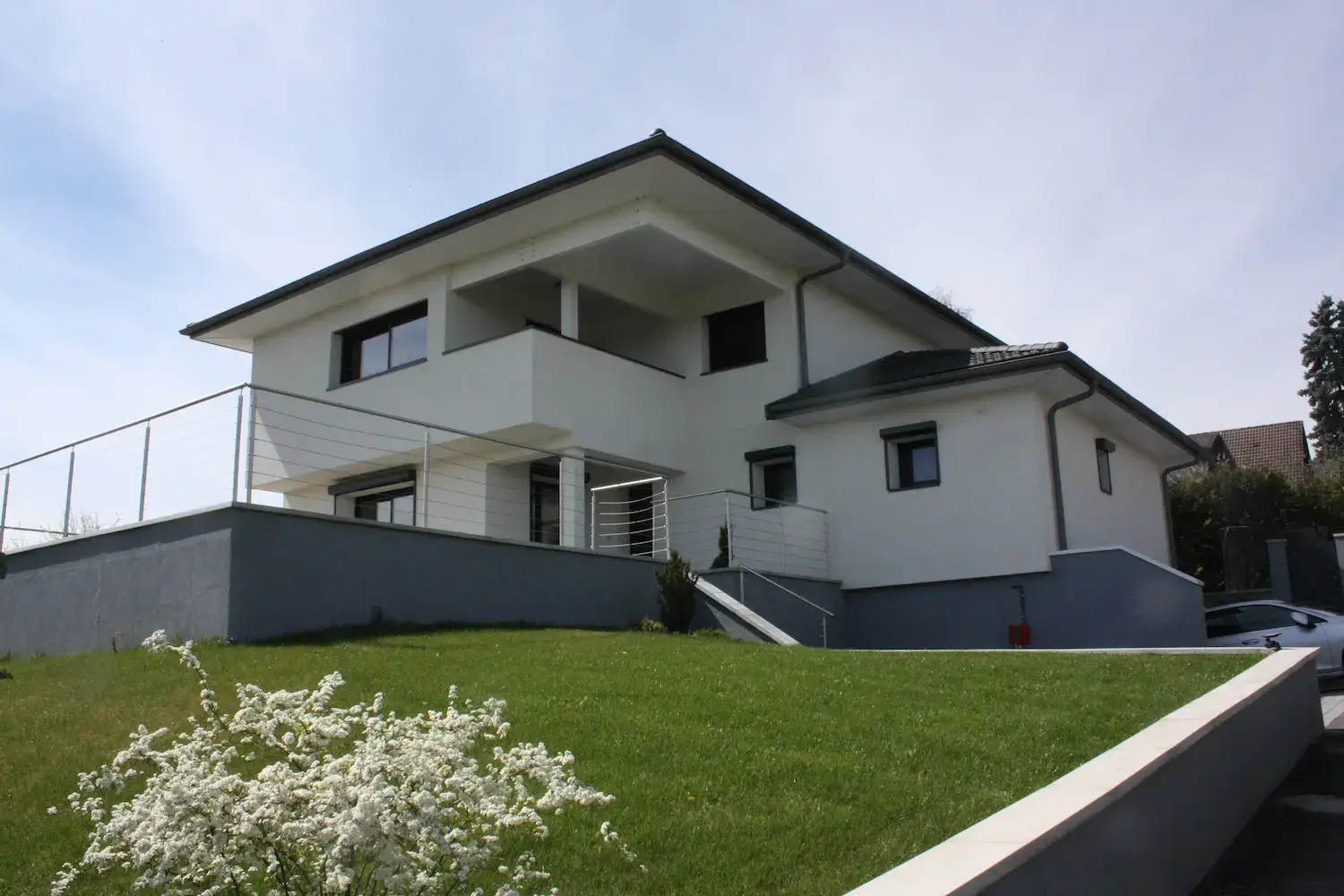 Maison après surélévation à Divonne-les-Bains — façade principale, balcon ossature bois, jardin fleuri — Jancu Architectes Pays de Gex Maison après surélévation à Divonne-les-Bains — façade principale, balcon ossature bois, jardin fleuri — Jancu Architectes Pays de Gex